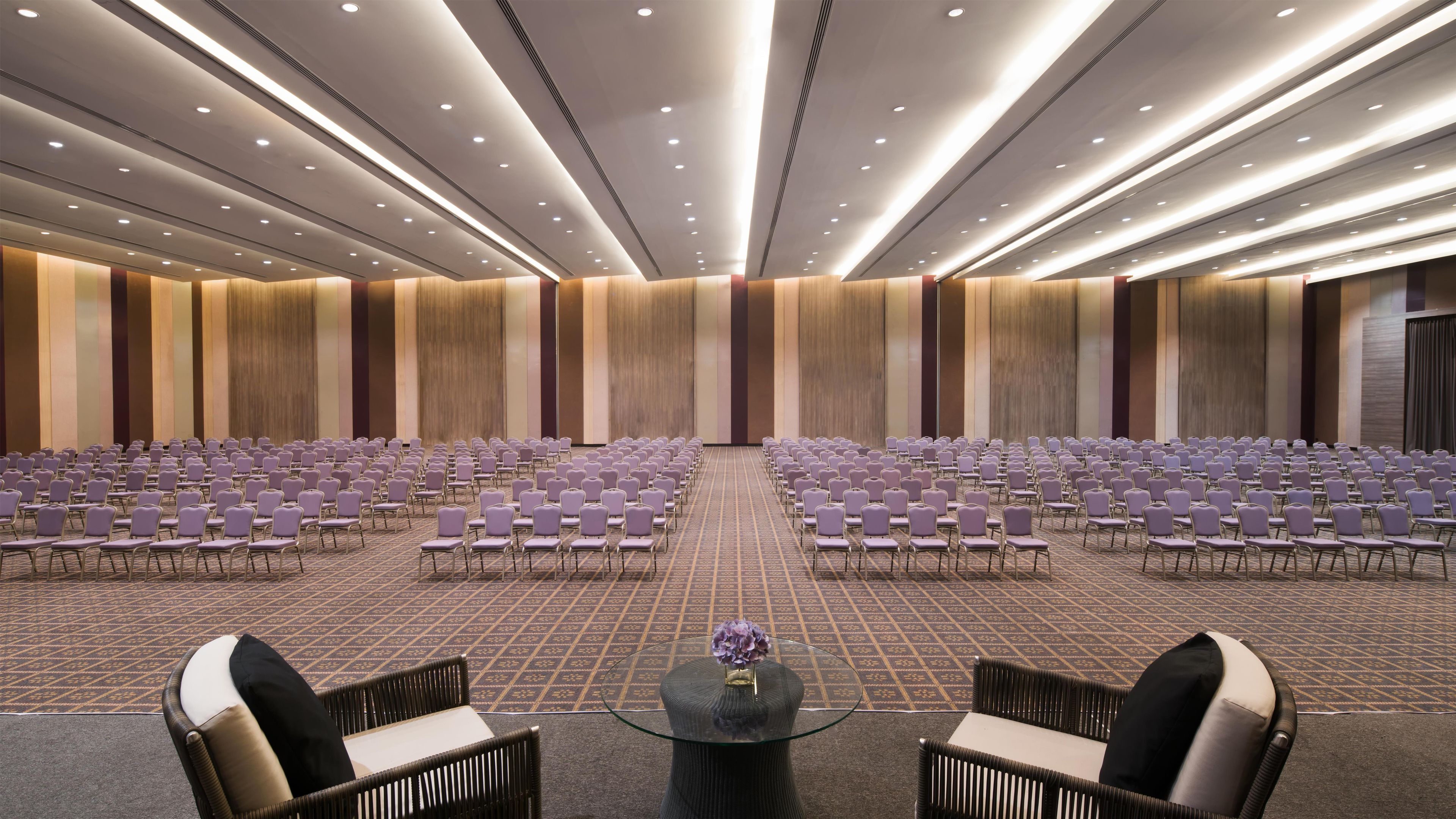 A conference room with rows of chairs, a glass table with a vase, and a patterned carpet.