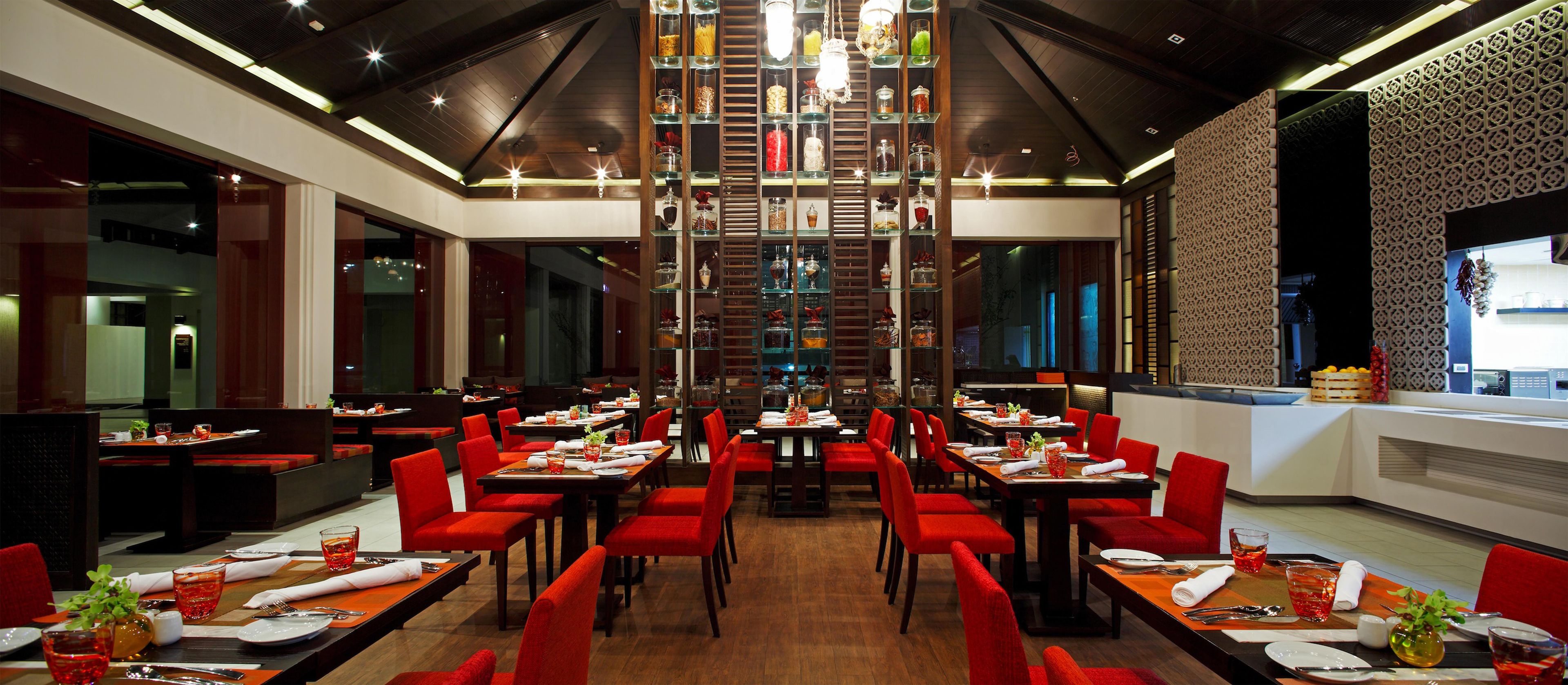 Un restaurante con varias mesas de comedor y sillas rojas, un candelabro decorativo en el centro, y una pared con diseño en un lateral.