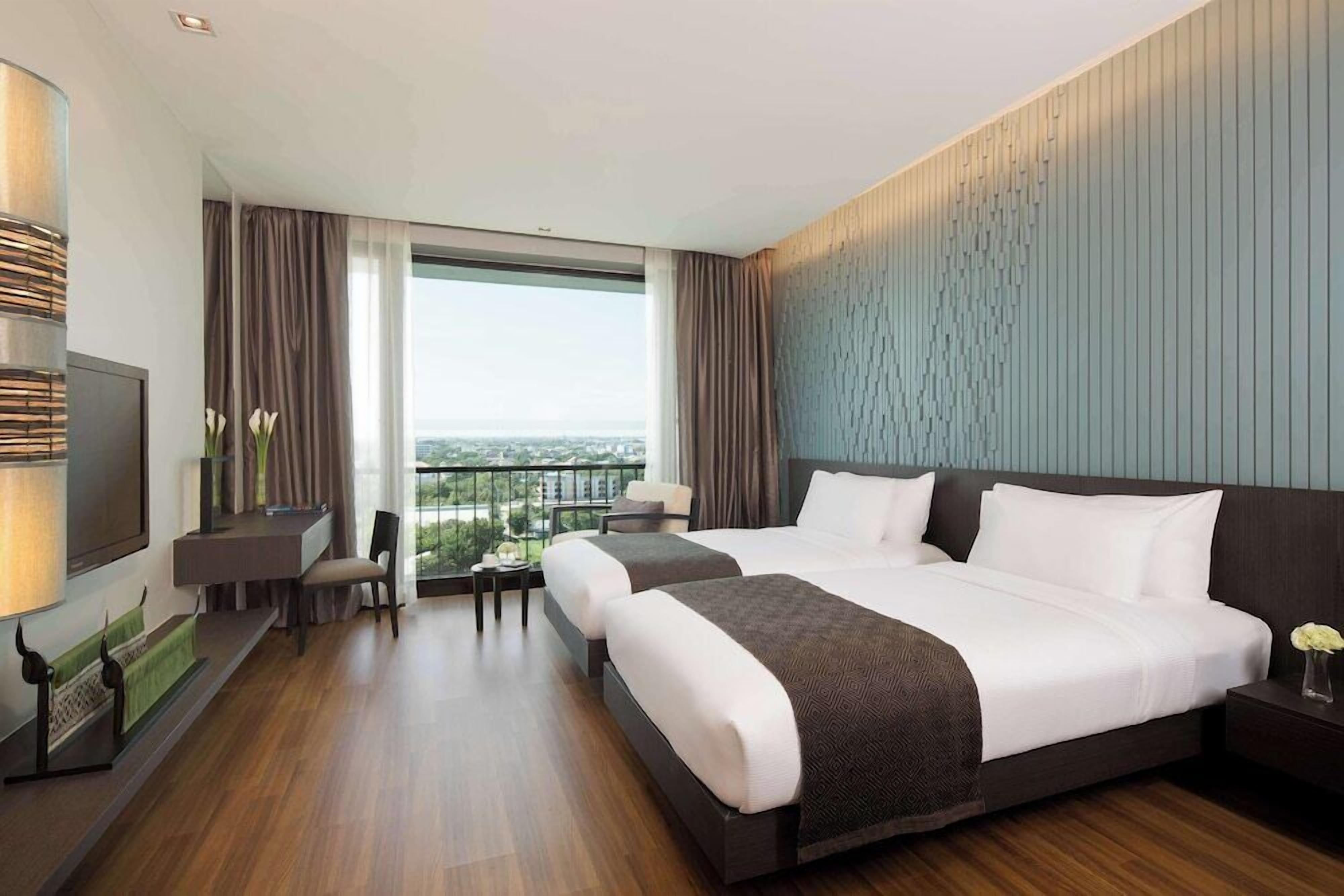 A hotel room with a large bed, a desk, a chair, a TV, and a view of the city.