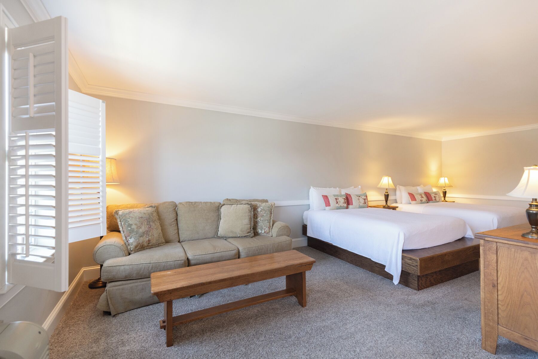 A bedroom with a sofa, two beds, a wooden bench, and bedside lamps.