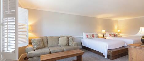 A bedroom with a sofa, two beds, a wooden bench, and bedside lamps.