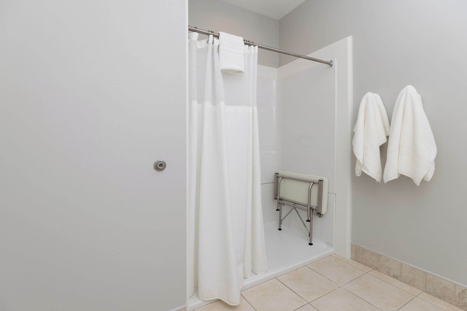 A bathroom with a shower, a towel rack, and a handrail.