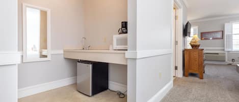 A compact, well-lit bathroom with a sink, mirror, and a small refrigerator.