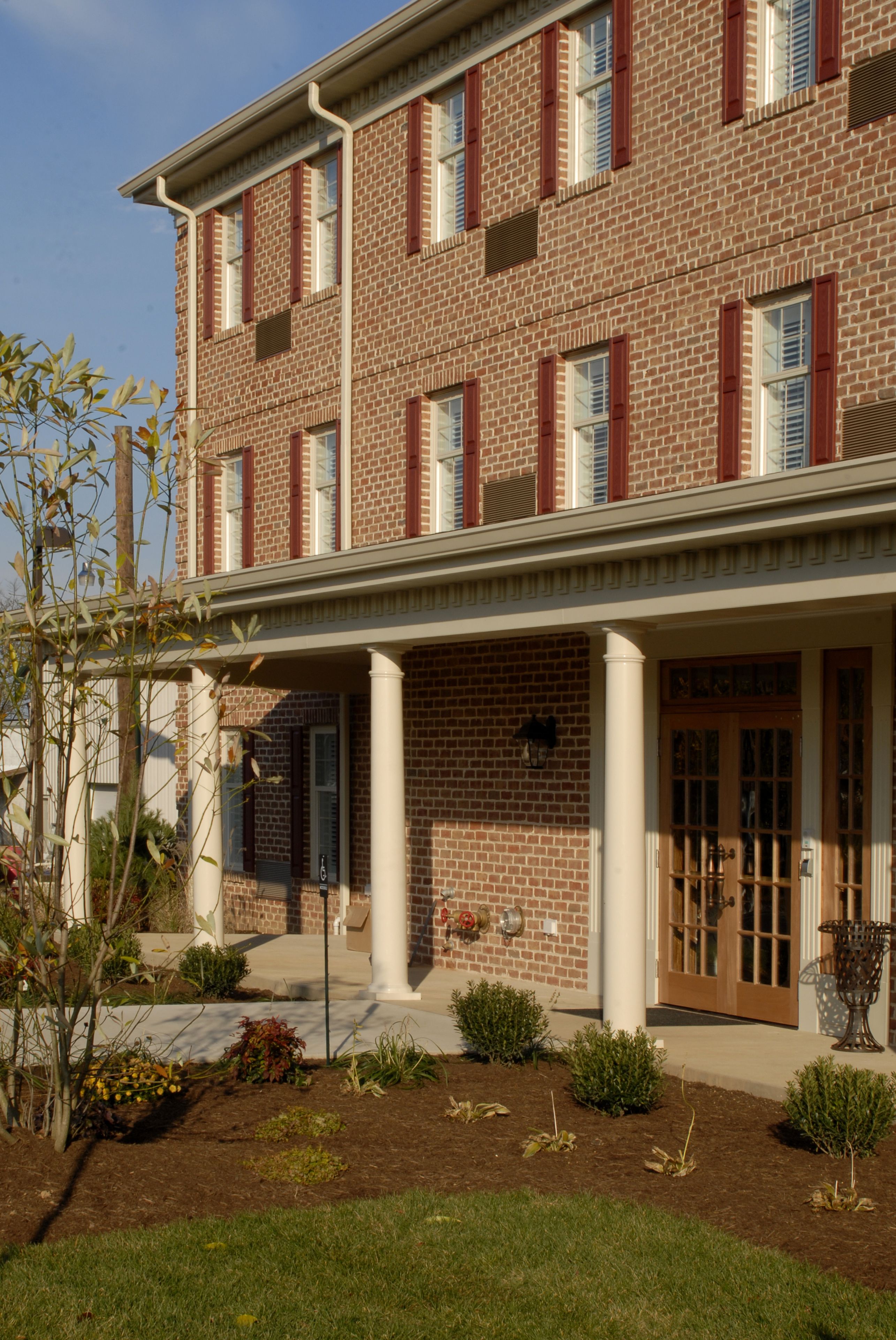 A multi-story brick building with a covered entrance and small potted plants.