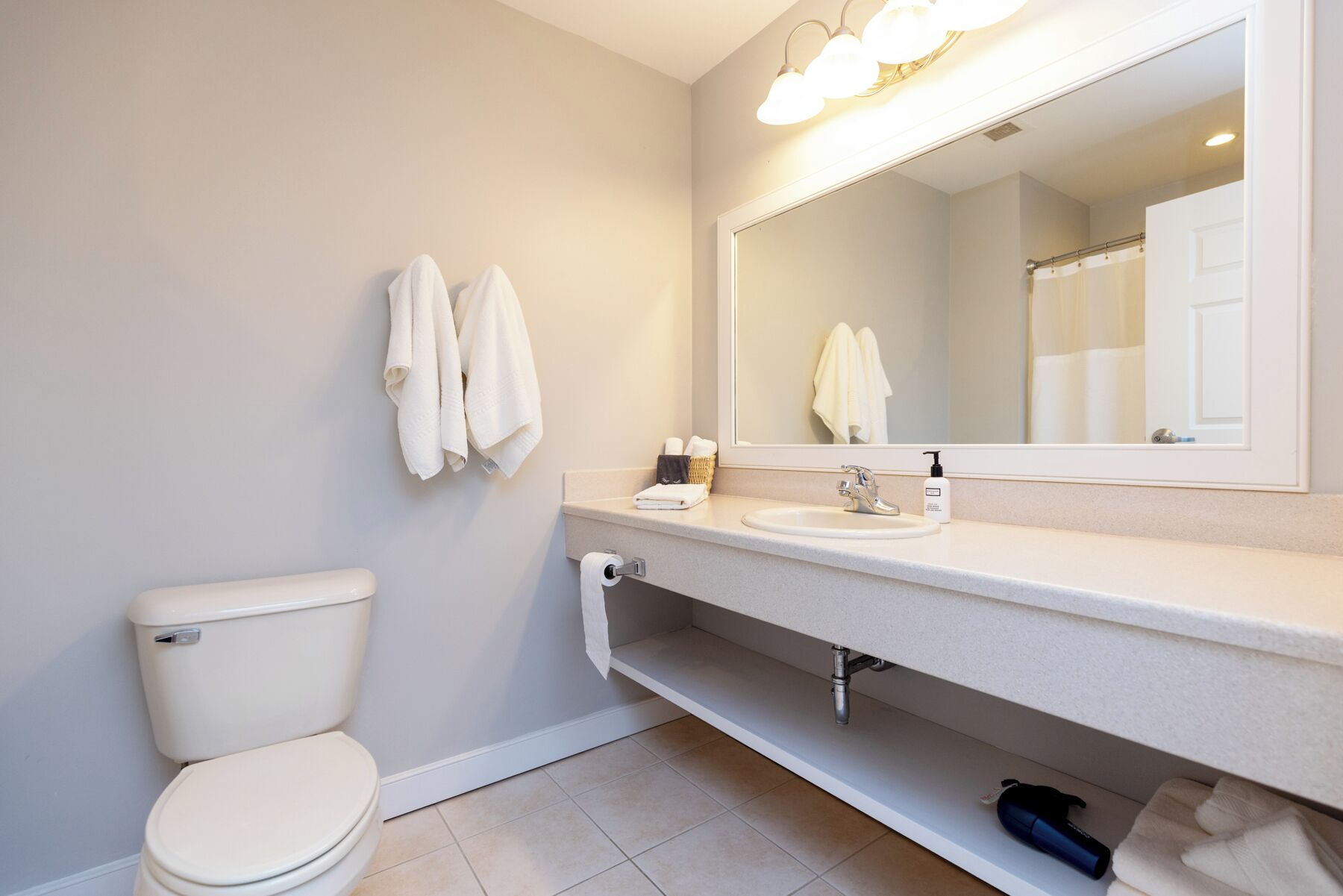 Une salle de bain moderne avec des toilettes, un lavabo et un miroir. Des serviettes sont accrochées au mur et un flacon de savon liquide est posé sur le lavabo.