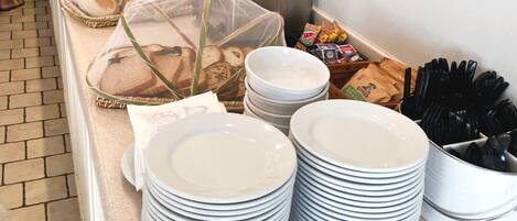 Montaje de bufé con pilas de platos blancos, alimentos cubiertos y un tostador.