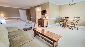 Een slaapkamer met een bed, een houten bankje, een eettafel met stoelen en een kaptafel.