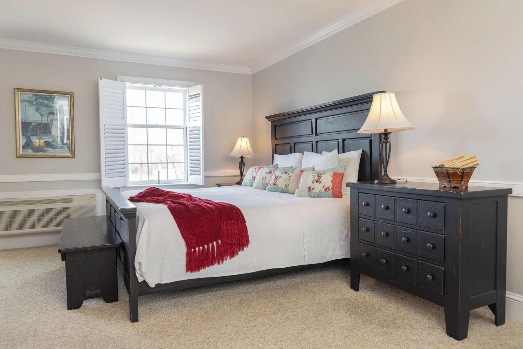 A bedroom with a bed, bedside tables, a dresser, a window with shutters, and a radiator.