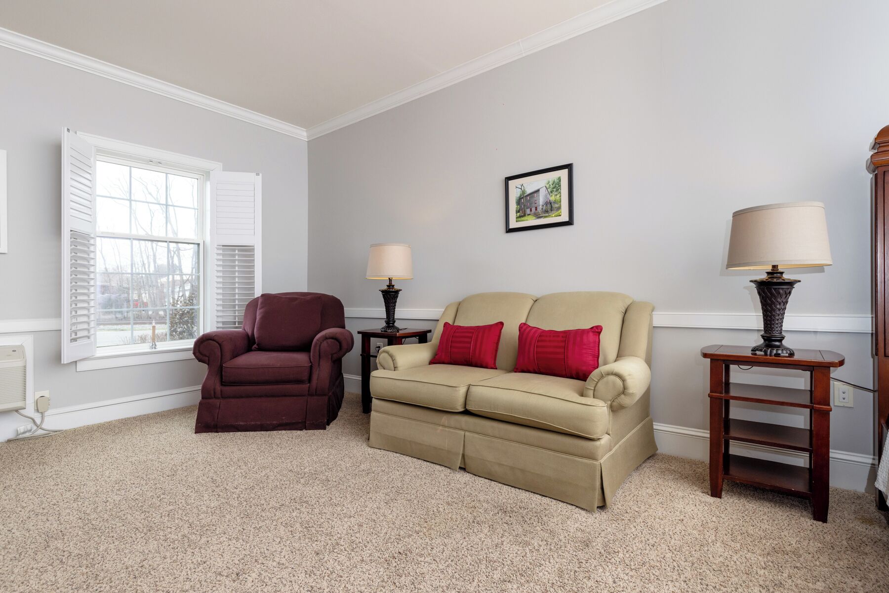 A living room with a beige sofa, a red armchair, two side tables with lamps, and a framed picture on the wall.