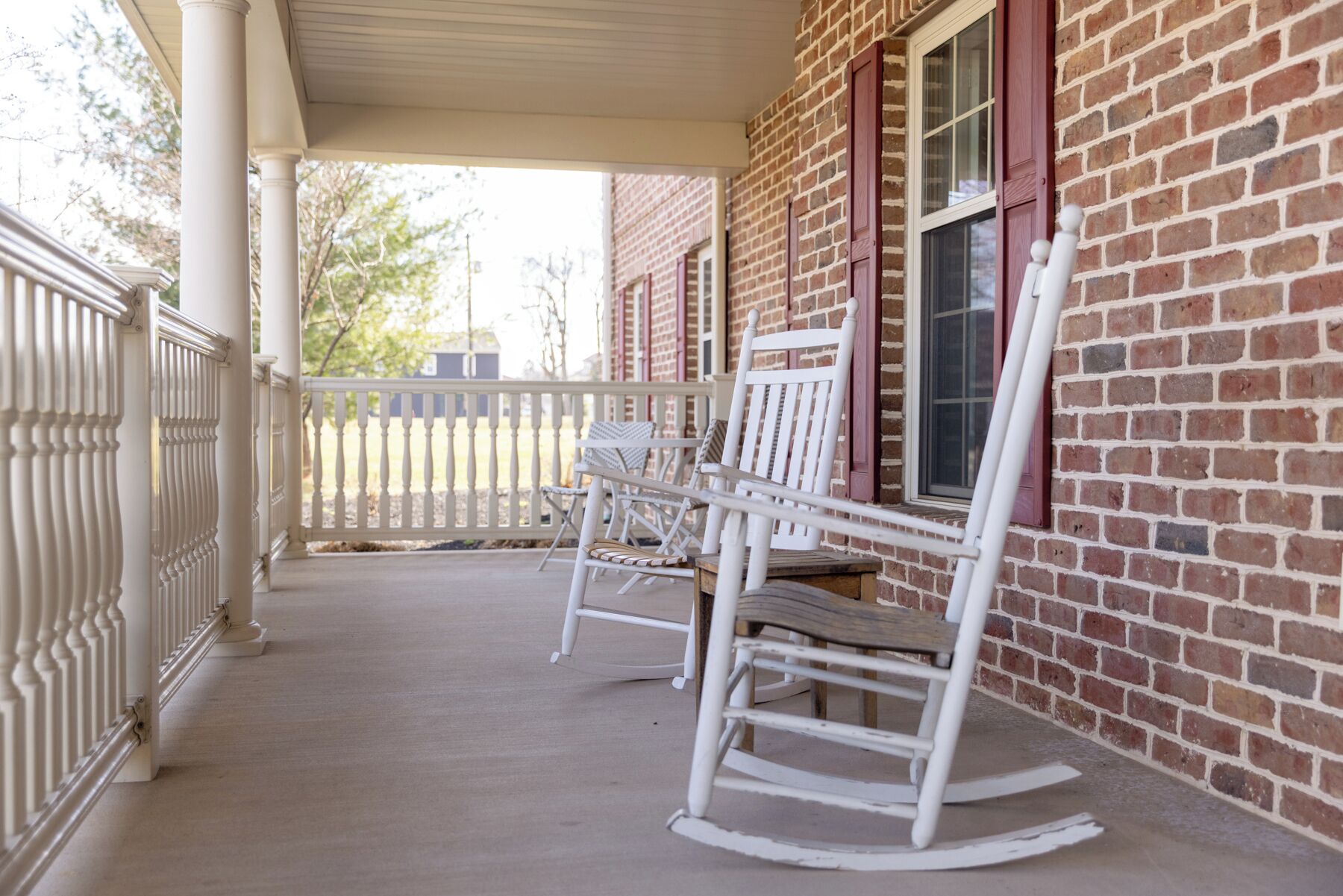 A porch with two rocking chairs, a brick wall, and a white railing.