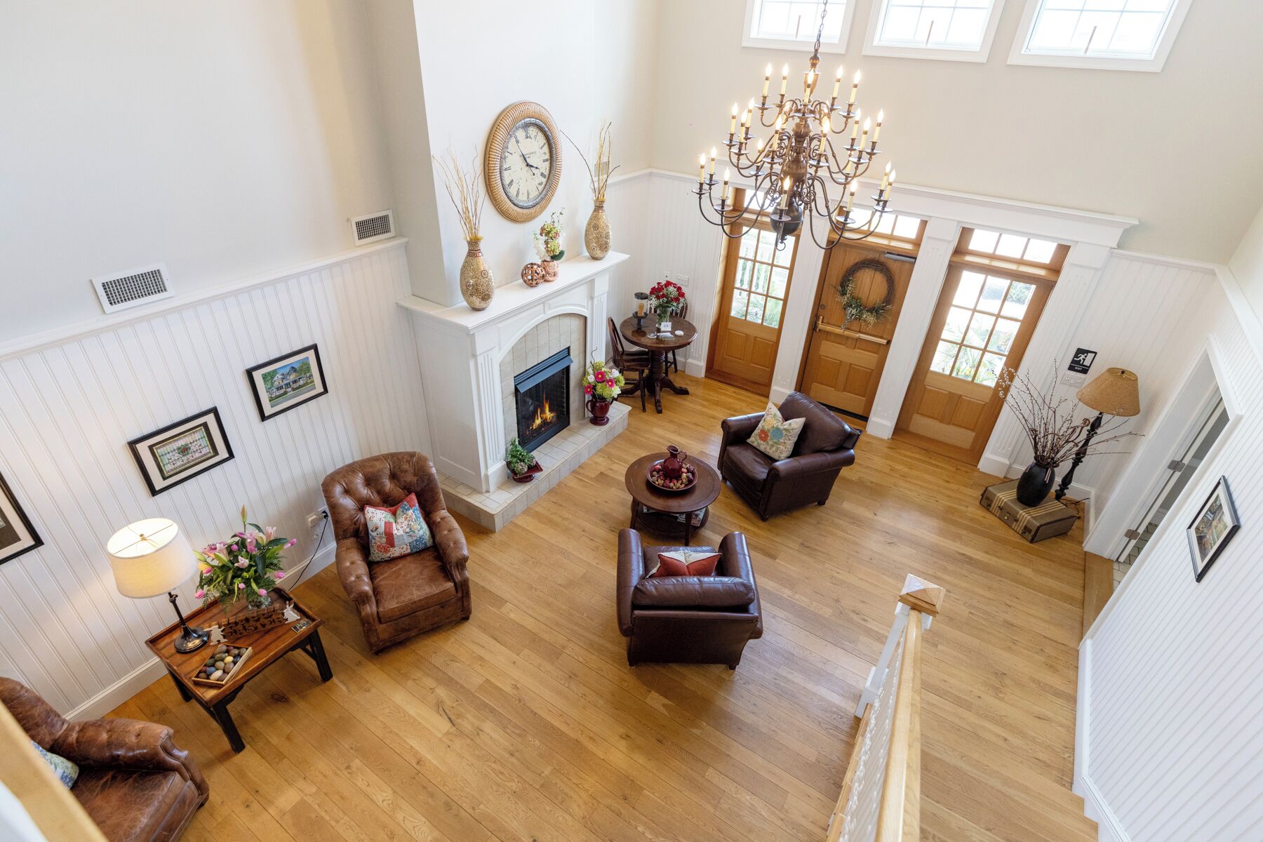 A spacious living room with a fireplace, leather sofas, a chandelier, and a view of the outdoors through large windows.