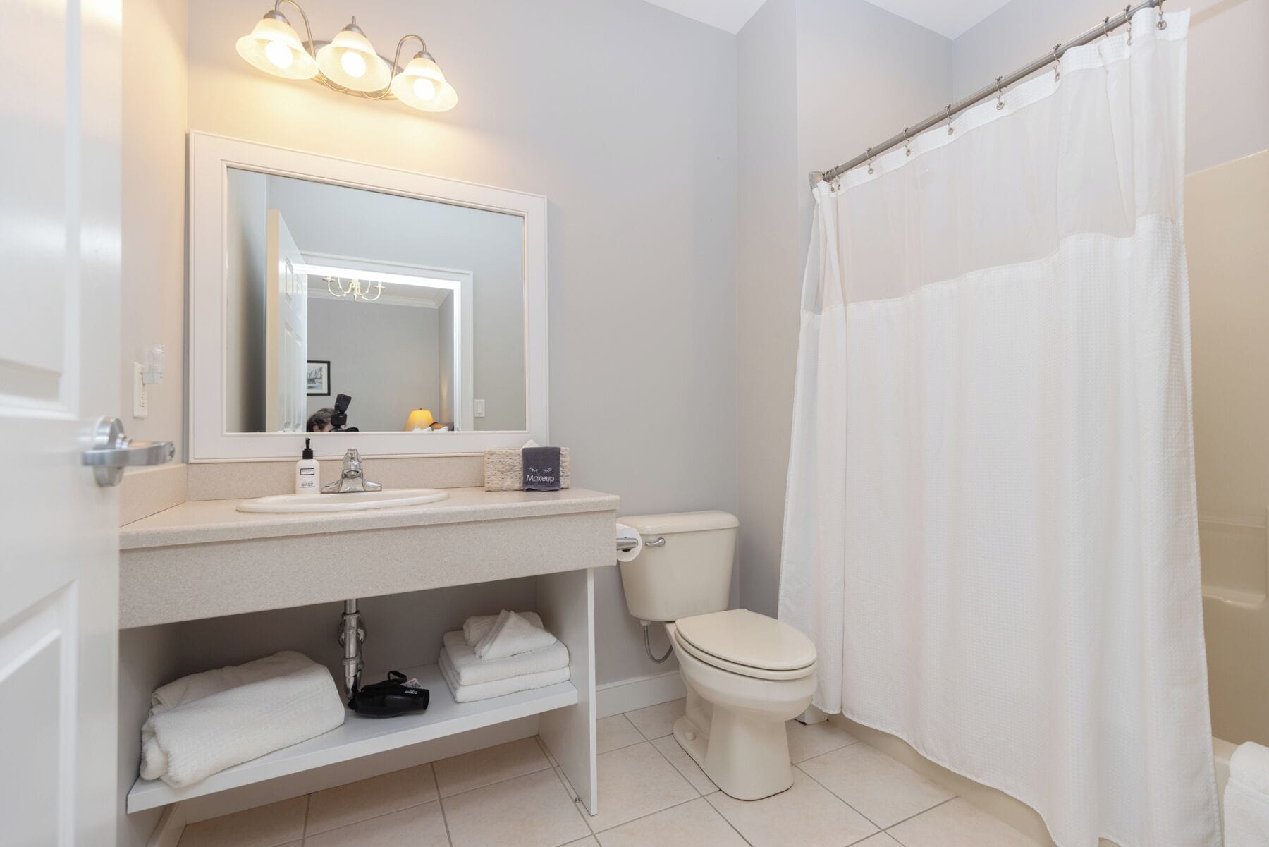 Une salle de bain avec un lavabo blanc, un miroir et des toilettes. On y trouve un porte-serviettes sous le lavabo et un rideau de douche.