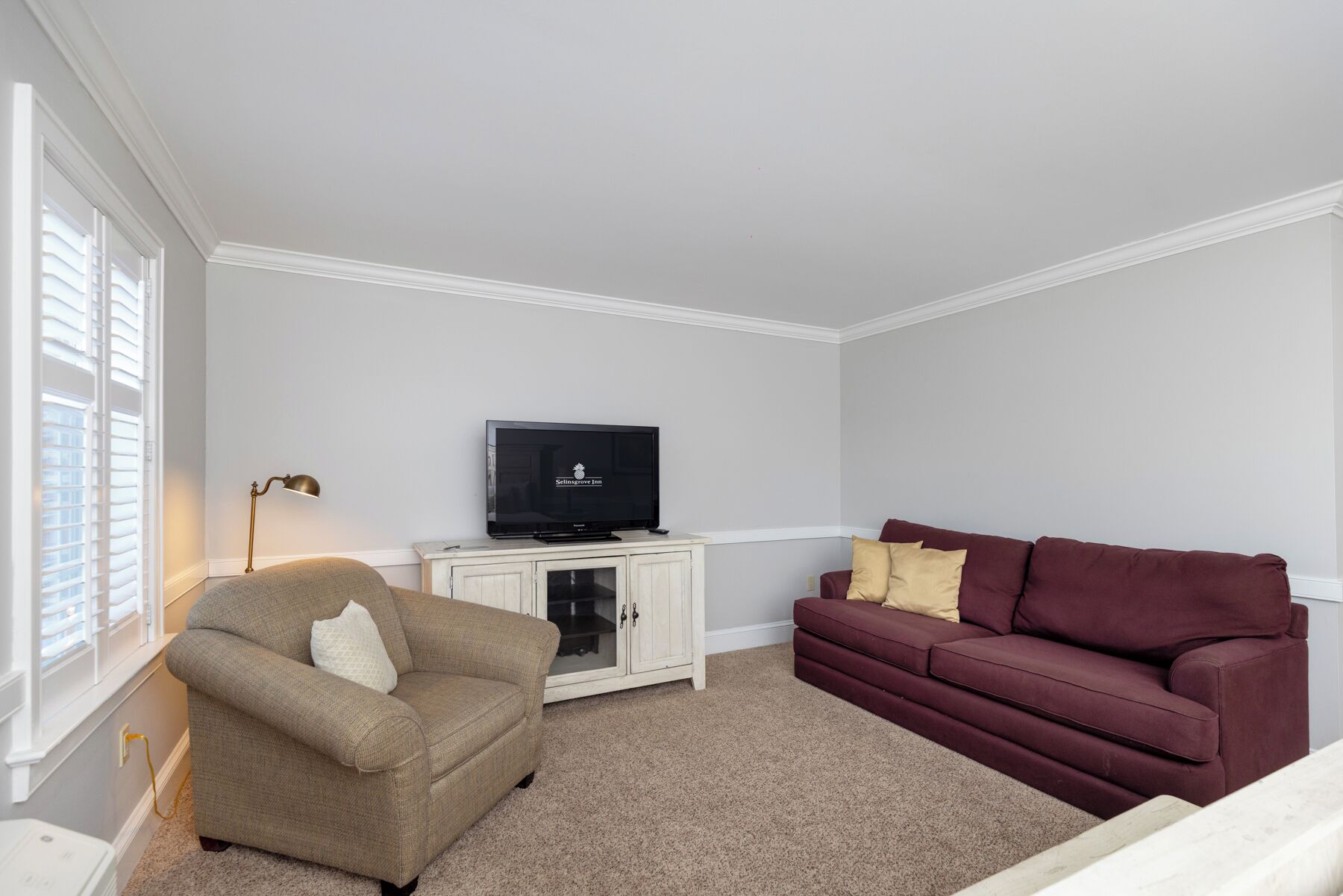 Un salón con un sillón color beige, un sofá rojo, un televisor sobre un mueble bajo y una lámpara.