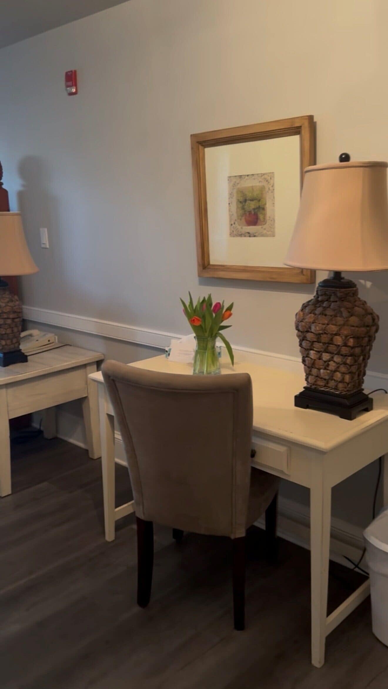 A dining area with a table, chairs, a lamp, and a vase with flowers.