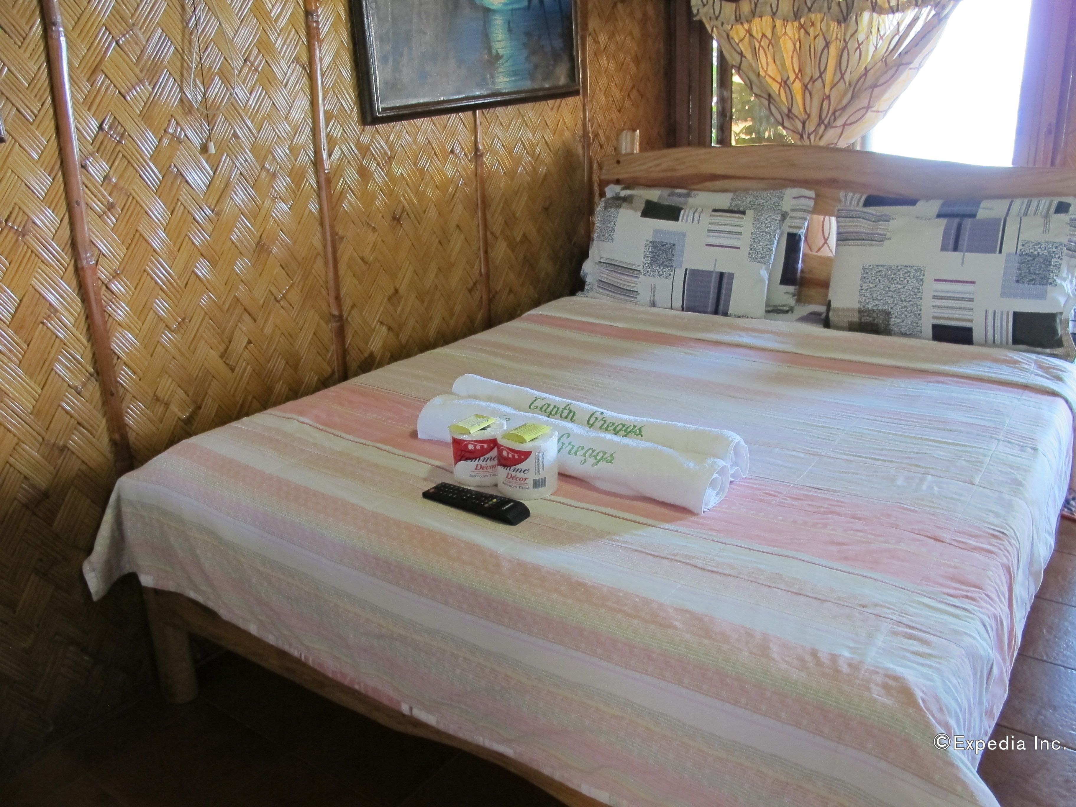 A neatly made bed with a striped bedspread, two rolled towels, a remote control, and decorative containers on the bed.