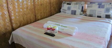 A neatly made bed with a striped bedspread, two rolled towels, a remote control, and decorative containers on the bed.