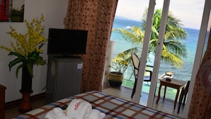A hotel room with a bed, a television, a potted plant, and a view of the ocean. - Capt'n Gregg's (Puerto Galera)