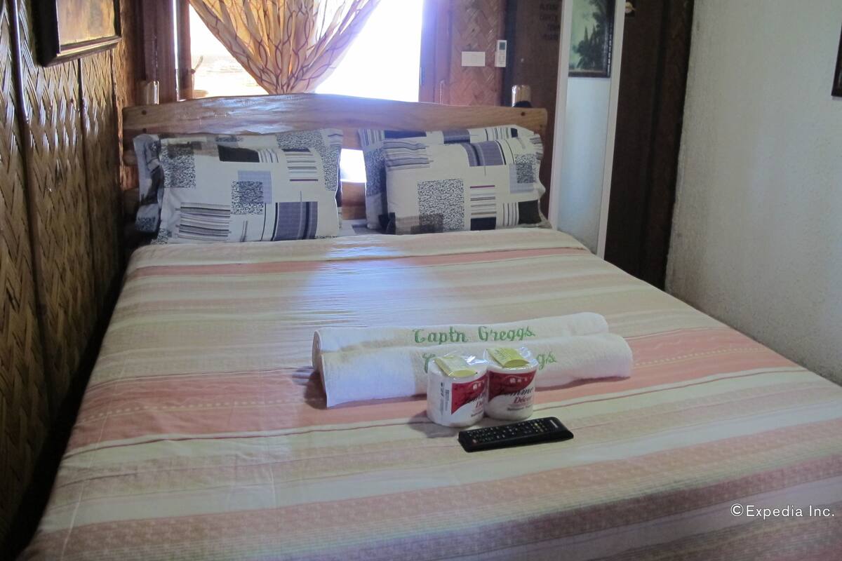 A neatly made bed with a striped bedspread, two rolled towels, and a remote control.