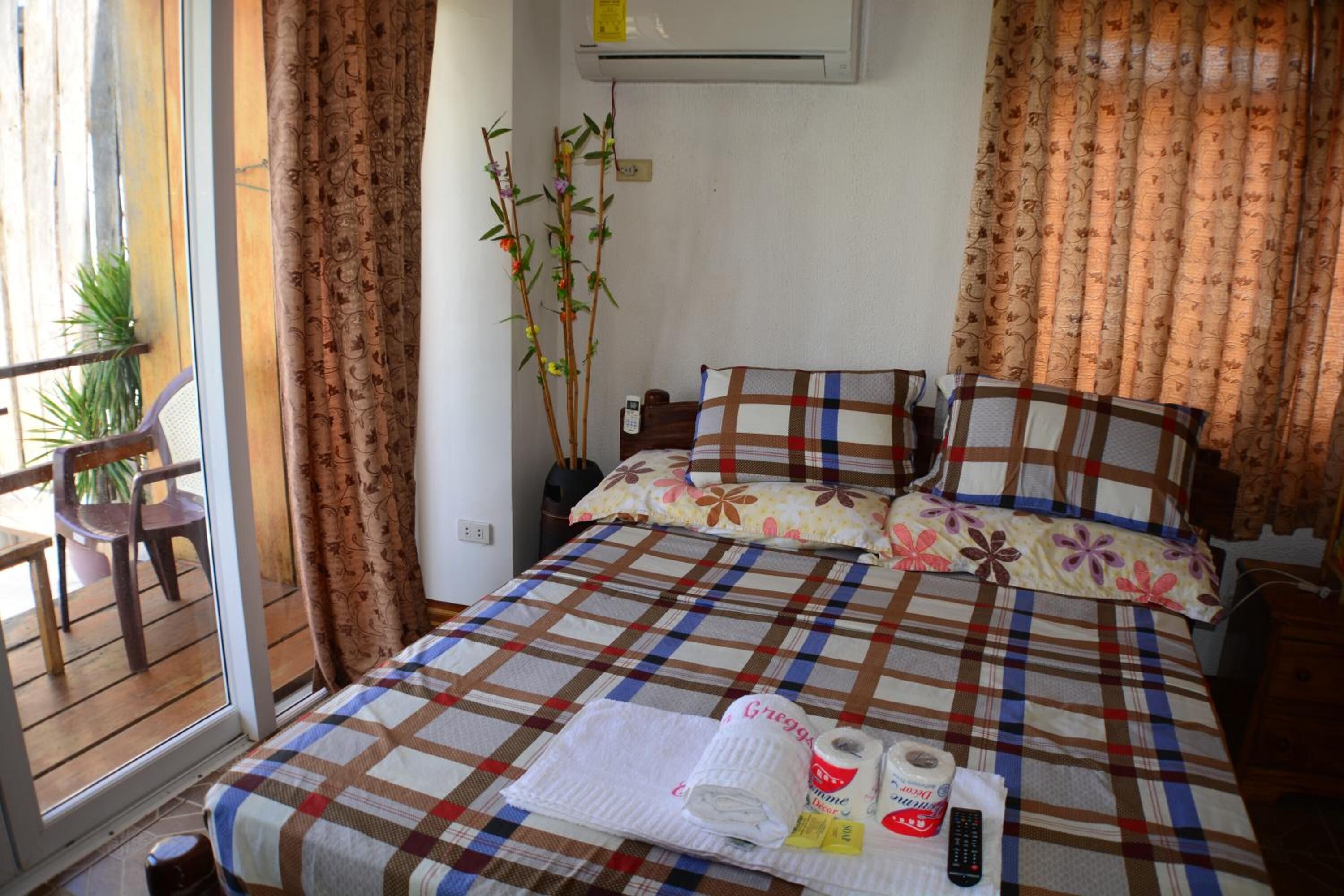 A hotel room with a bed, a chair, a potted plant, and a window with curtains.