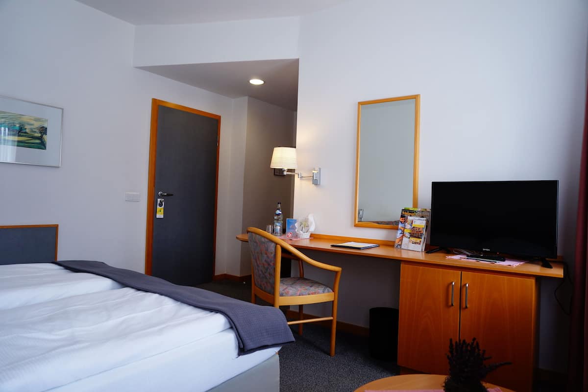 A hotel room with a bed, a desk with a chair, a television, and a mirror.