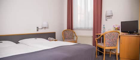 Habitación de hotel con dos camas, un escritorio con computadora, una silla, una lámpara y una ventana con cortinas.