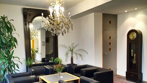 A lobby with black leather seating, a chandelier, a large mirror, and a clock on the wall. - Ringhotel Altstadt (Guestrow)