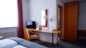A hotel room with a bed, a desk with a computer, a TV, a mirror, and a wardrobe. - Ringhotel Altstadt (Guestrow)