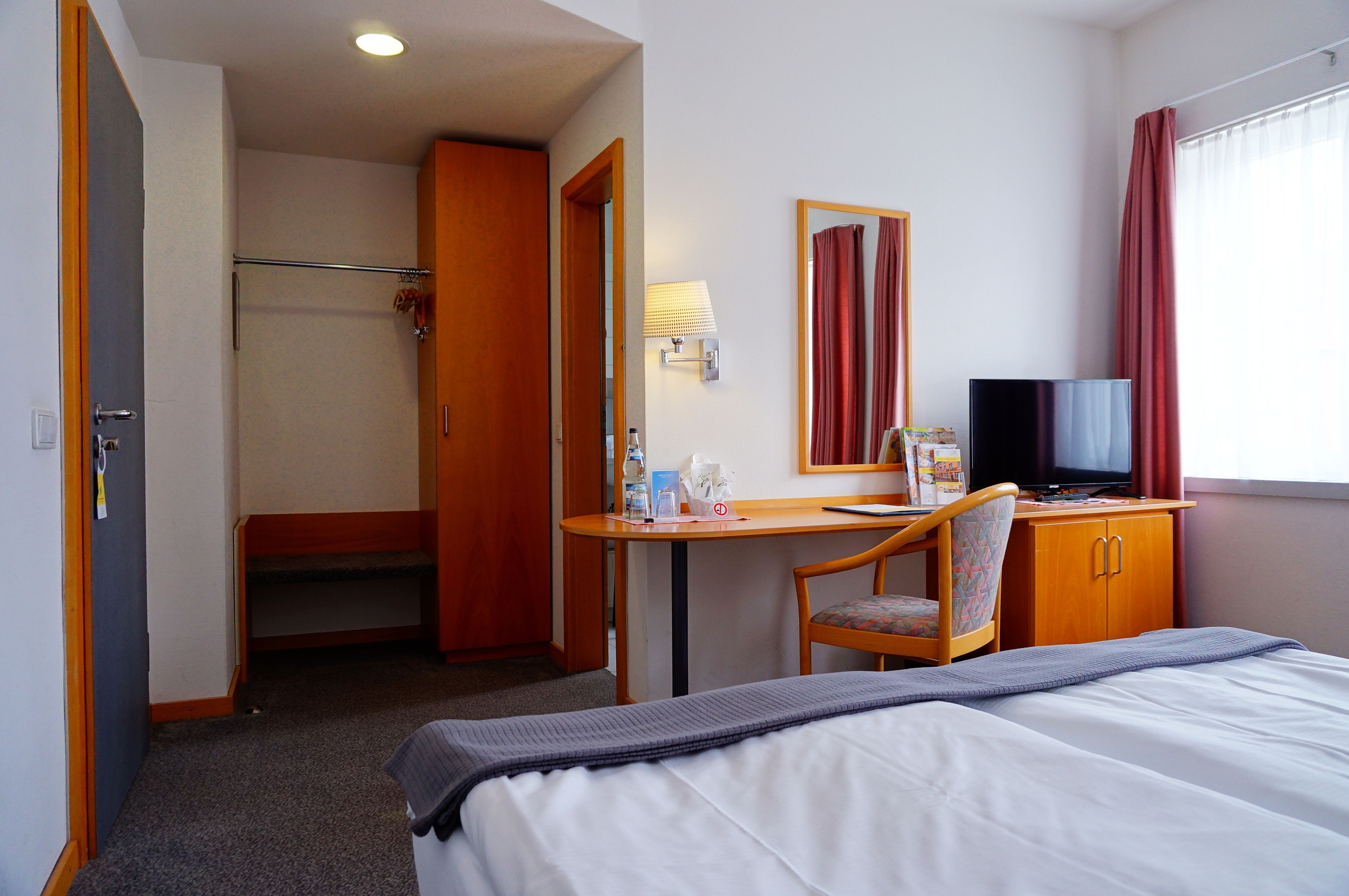 Habitación de hotel con cama, escritorio con silla, televisión y baño con ducha.