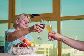 A person toasting with another at a table with a basket of fruits. - AG Hotel (Abu Dhabi)