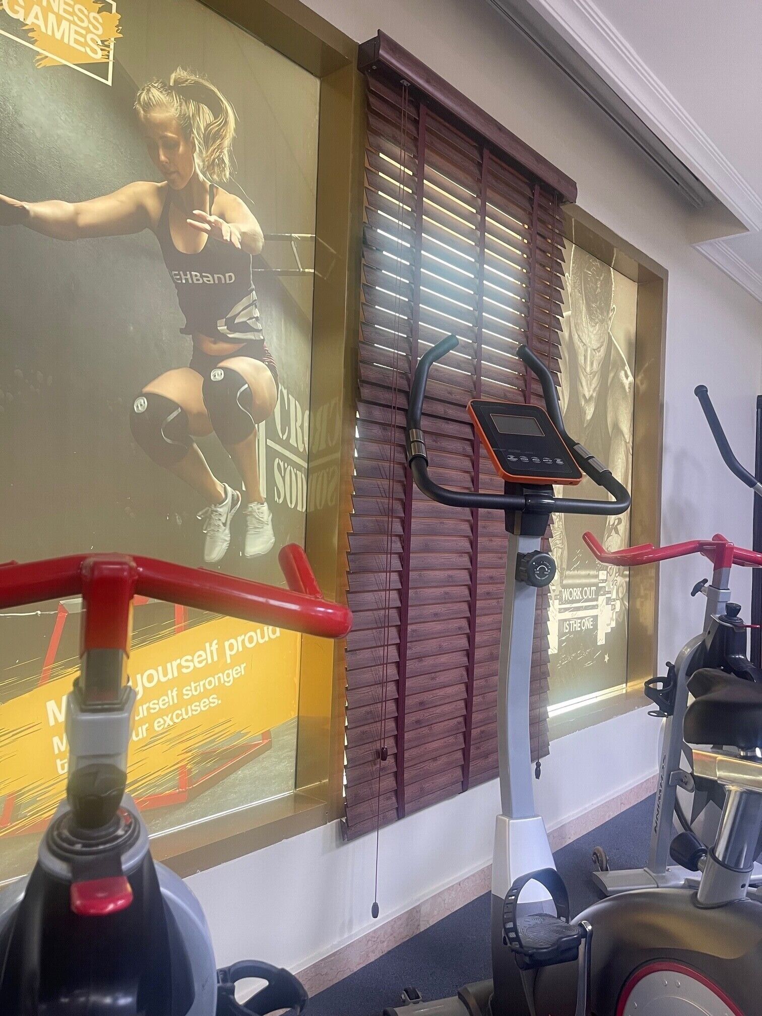 A gym with exercise equipment, a large motivational poster, and wooden blinds.