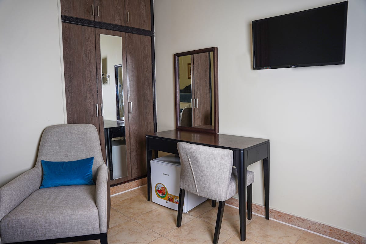 A room with a desk, chair, wardrobe, and a television on the wall.