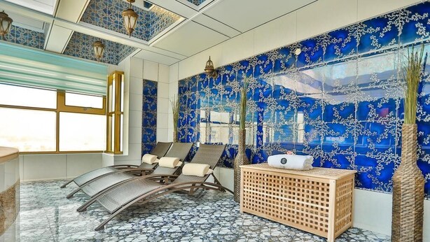 A room with a blue patterned wall, a window, a seating area with chairs, and a wooden side table. - AG Hotel (Abu Dhabi)