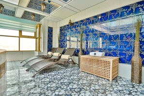 A room with a blue patterned wall, a window, a seating area with chairs, and a wooden side table. - AG Hotel (Abu Dhabi)