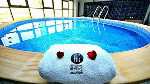 An indoor swimming pool with clear blue water, a wooden deck, and a towel with a logo and text. - AG Hotel (Abu Dhabi)