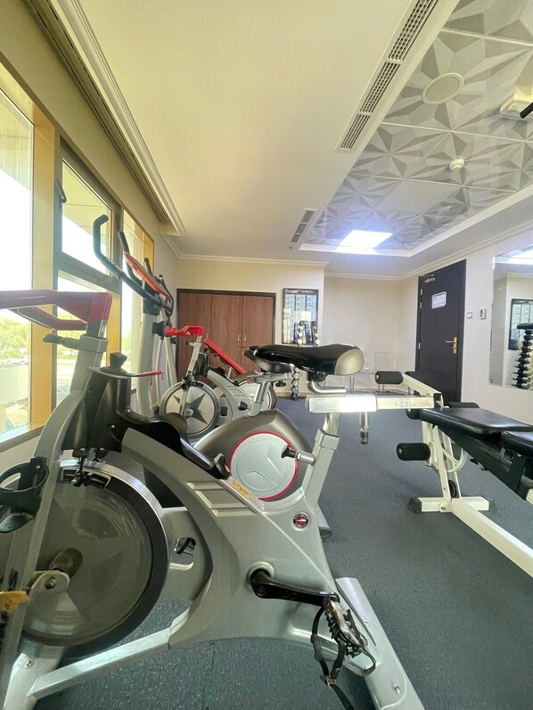 Une salle de sport équipée de divers appareils d’exercice, dotée d’une grande fenêtre et d’une porte.