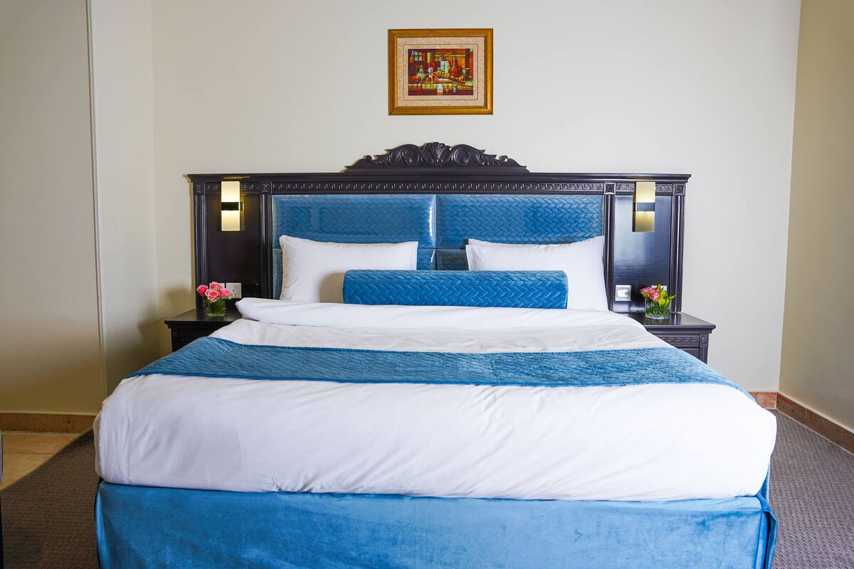 A neatly made bed with blue and white bedding, a wooden headboard, and a framed picture above it.