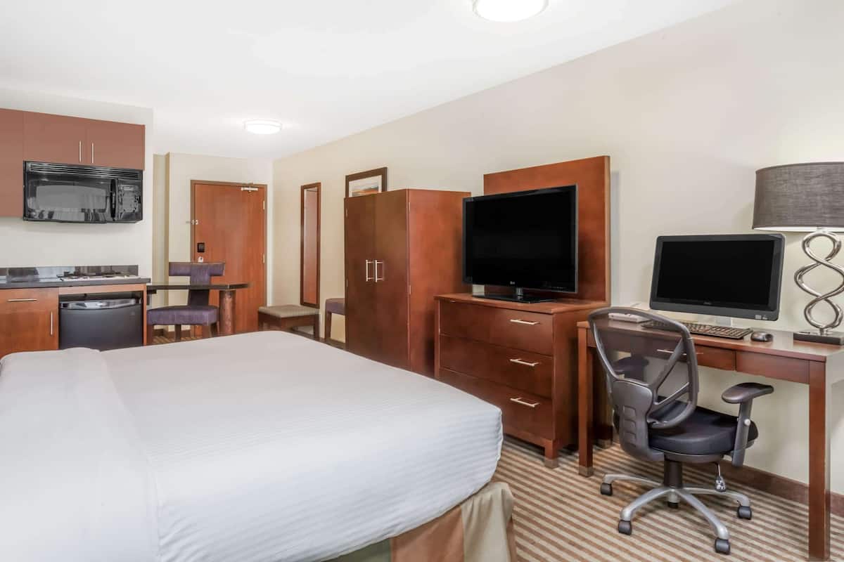 A hotel room with a bed, a desk with a computer, a TV, and a microwave.