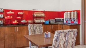 Una cocina con salpicadero rojo, un microondas, un tostador y varios alimentos en estantes.