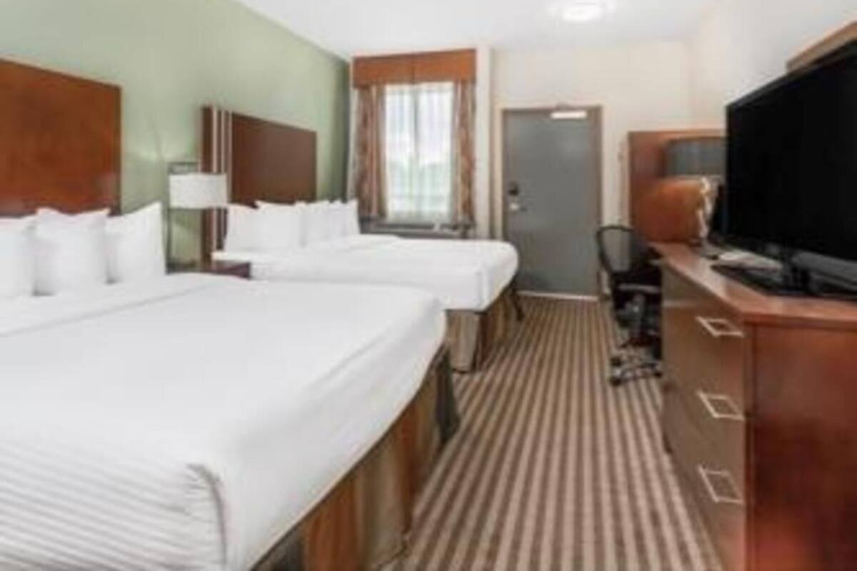 A hotel room with two beds, a television, a desk, and a window.