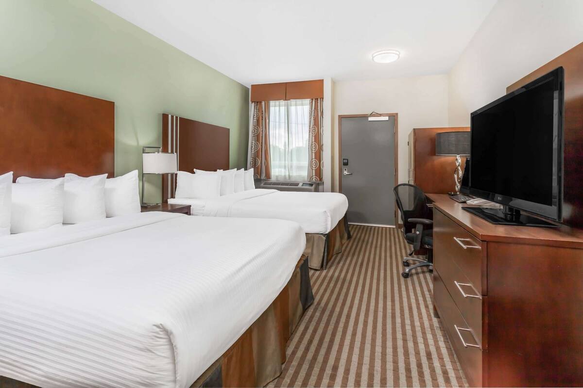 A hotel room with two beds, a desk with a flat-screen TV, a chair, and a door.