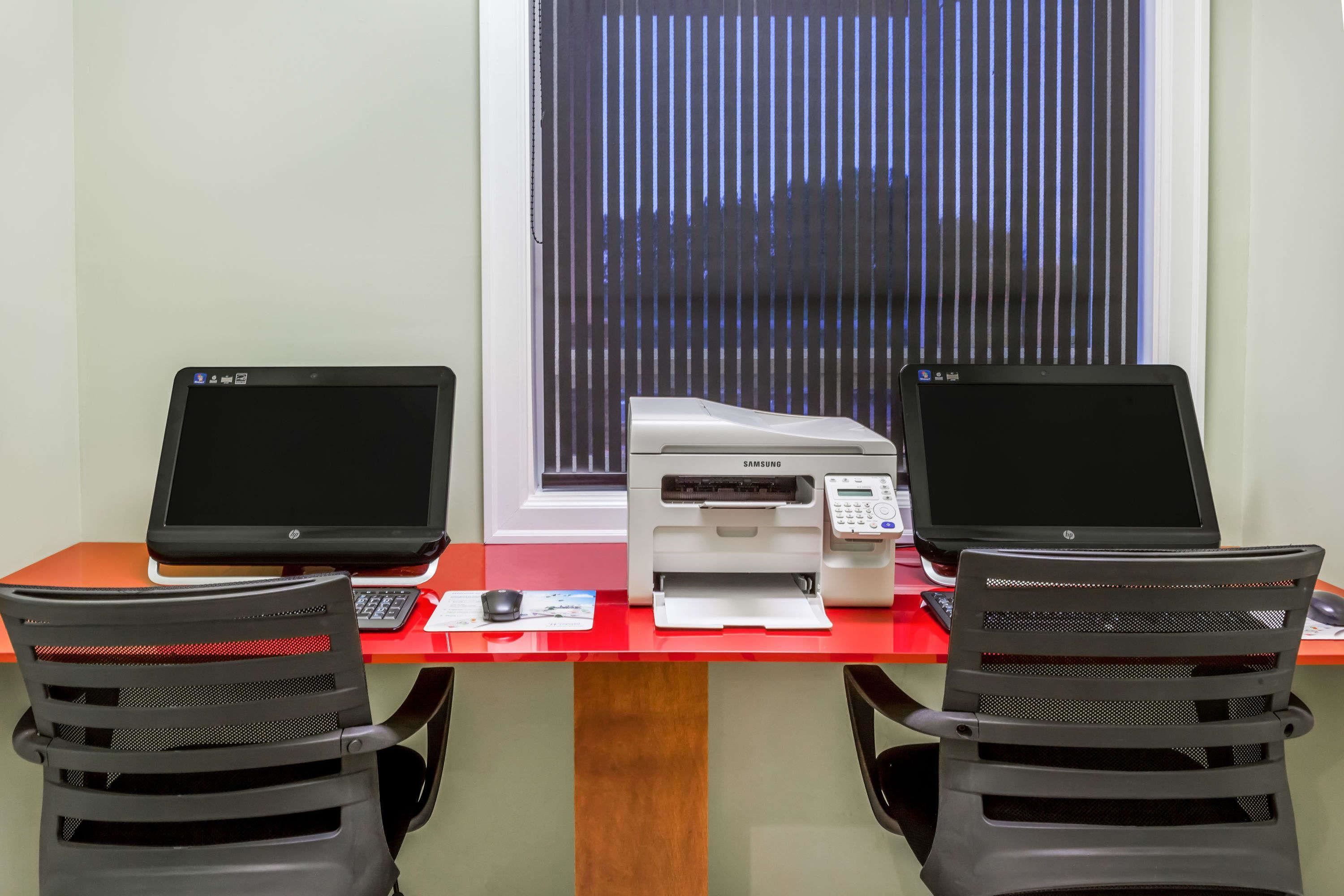 Un espacio de trabajo con dos computadoras portátiles HP, una impresora Samsung y dos sillas de oficina negras.