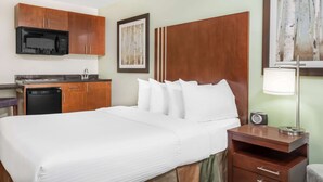 Una habitación de hotel con cama, escritorio con lámpara, microondas y lavamanos.