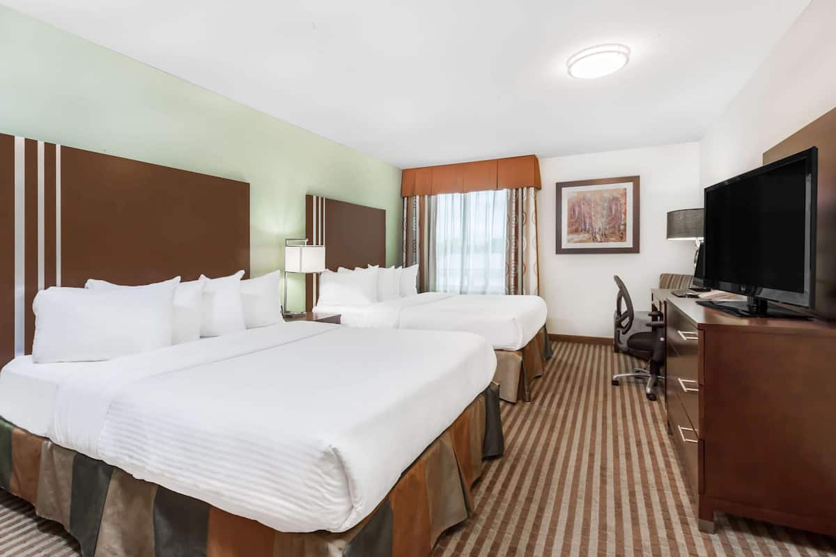 A hotel room with two beds, a desk, a TV, and a painting on the wall.