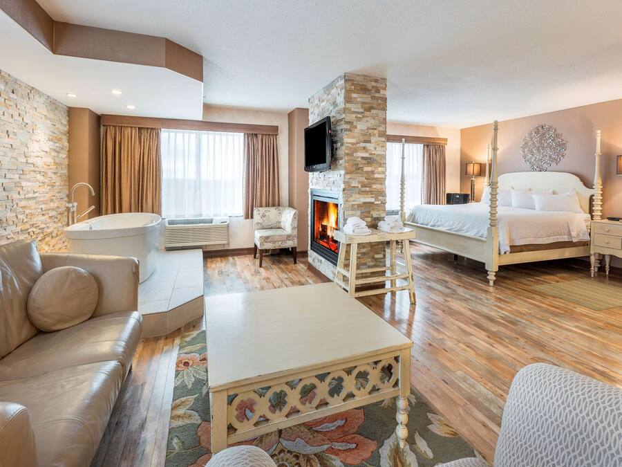 A hotel room with a stone wall, a fireplace, a bed, a sofa, a coffee table, and a TV.