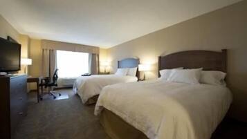 A hotel room with two beds, a desk, a chair, a television, and a window with curtains.