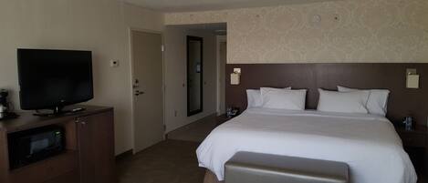 Habitación de hotel con una cama grande, televisión de pantalla plana, minibar y puerta de baño.