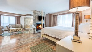 A hotel room with a large bed, a stone fireplace, a sofa, and a television. - Hampton Inn by Hilton Sydney (Sydney)
