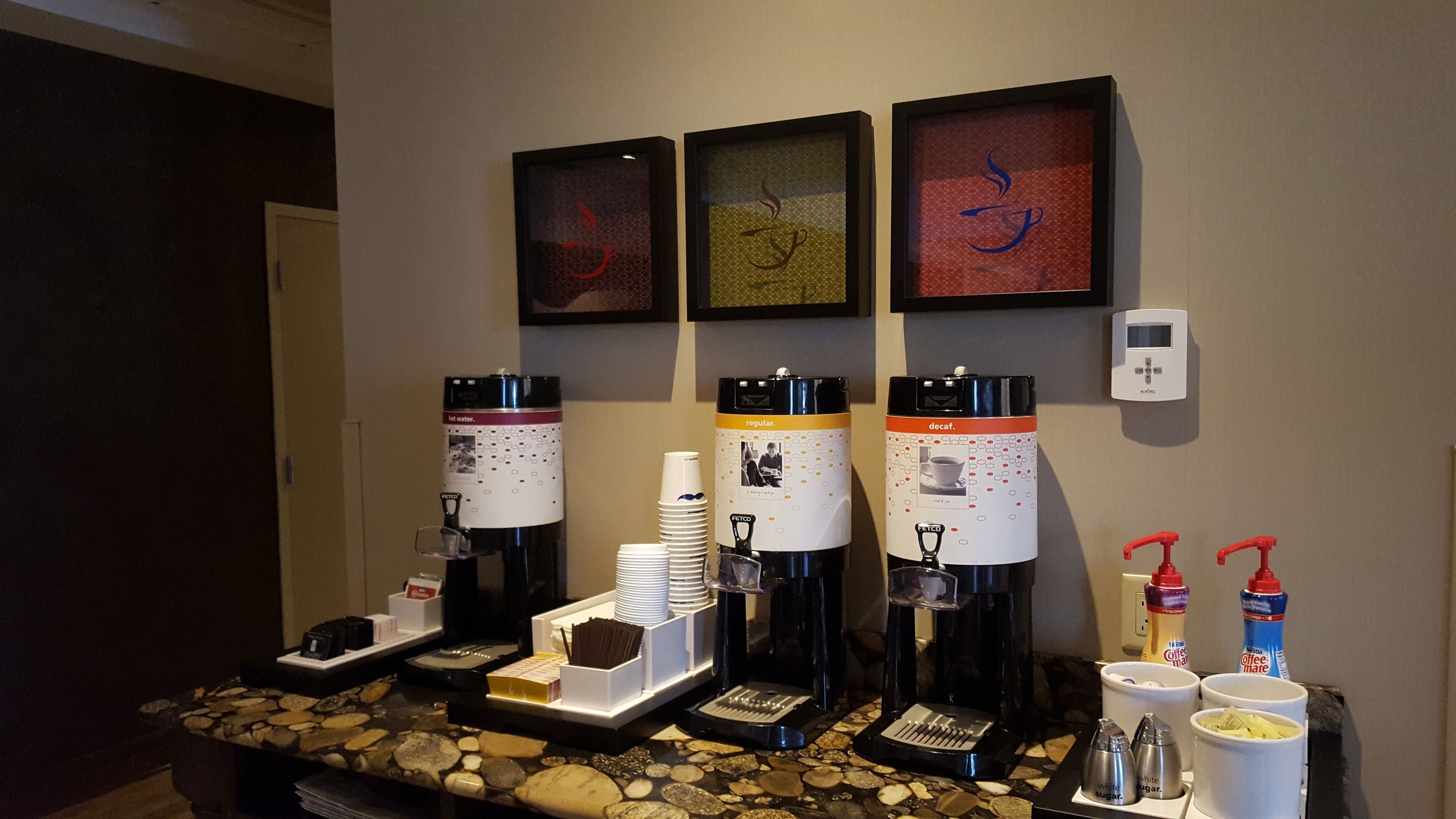 A coffee station with four coffee makers, disposable cups, and sugar and creamer dispensers.