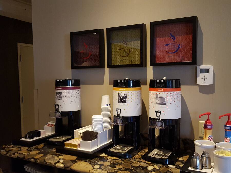 A coffee station with four coffee makers, disposable cups, and sugar and creamer dispensers.