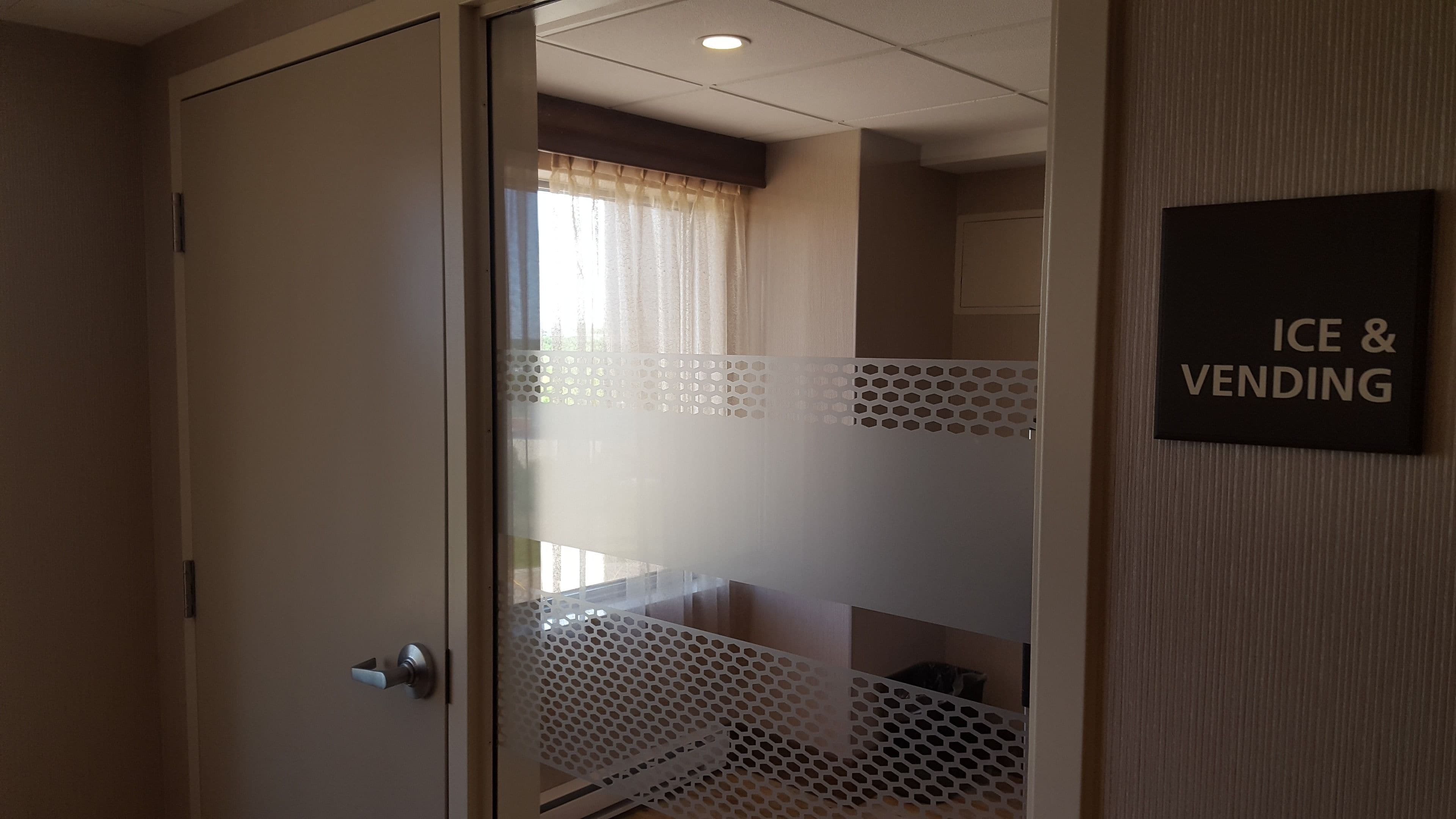 A hotel room with a sliding door leading to a balcony. A sign on the wall indicates the presence of an ice and vending machine.